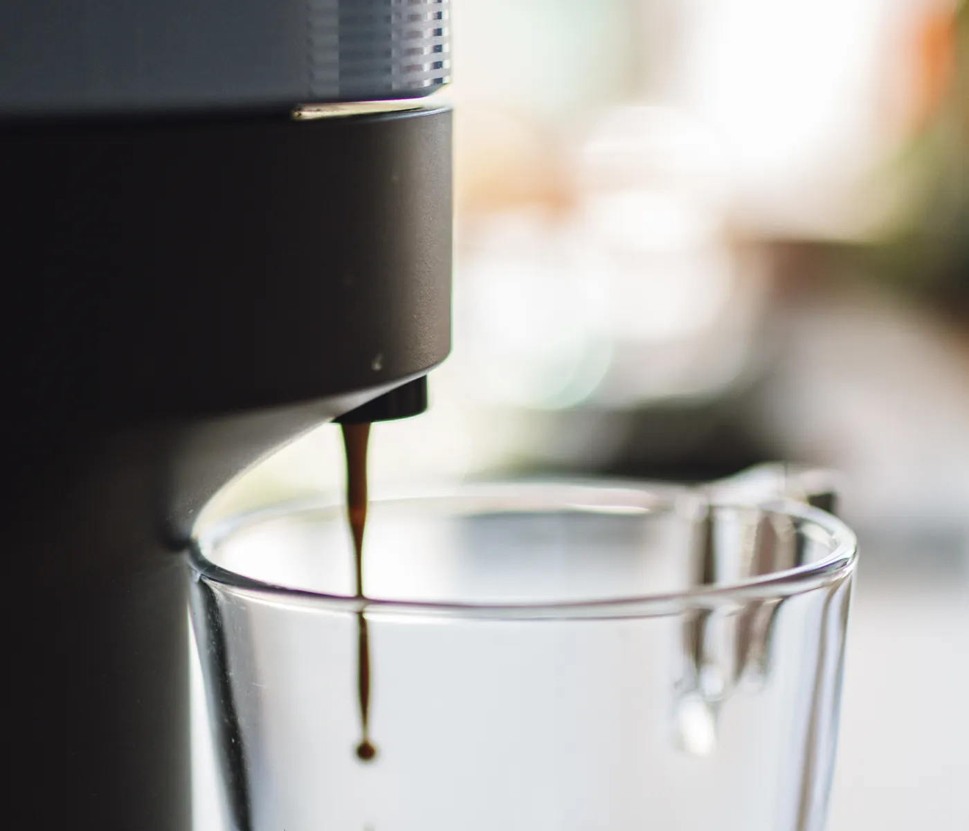 Fresh coffee dripping into a glass cup on a bright home kitchen counter